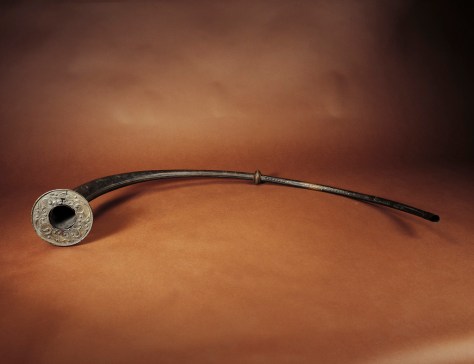  Trumpet, Loughnashade, Co. Armagh. Early Iron Age, first century bc. Found in a former lake, the Loughnashade, Co. Armagh trumpet is the only one to survive of a hoard of four found originally. Classical writers have left accounts of the unnerving effect on Roman armies which the continental Celts achieved by blowing their war trumpets before battle and we can assume a similar martial function for the splendid trumpet from Loughnashade. However, it is likely that the trumpet was also used on ceremonial and ritual occasions. It consists of two curved tubes, the joining of which is concealed by a ridged ring. At the flared mouth there is a decorated ring and its ornament is executed in the repousse technique, based on the classical lotus-bud motif. The quadrants are mirror images of each other and the design is composed of long, sinuous tendrils which terminate in spiral bosses in high relief. A number of trumpet curves are incorporated into the design. Both tubes are riveted along their length. One tube, which is clearly a later replacement, is poorly executed, while the other is a masterpiece of the riveterâ€™s craft, the quality being only matched occasionally on other fine metalwork such as the Petrie Crown and the Cork Horns. W8. L. along convex edge 186.5 cm; D. of mouth 19.3 cm. Browne 1800, 11â€“12; Kelly 1983, no. 31; Raftery 1983, no. 781, 239â€“40; Raftery 1984, 134â€“43.